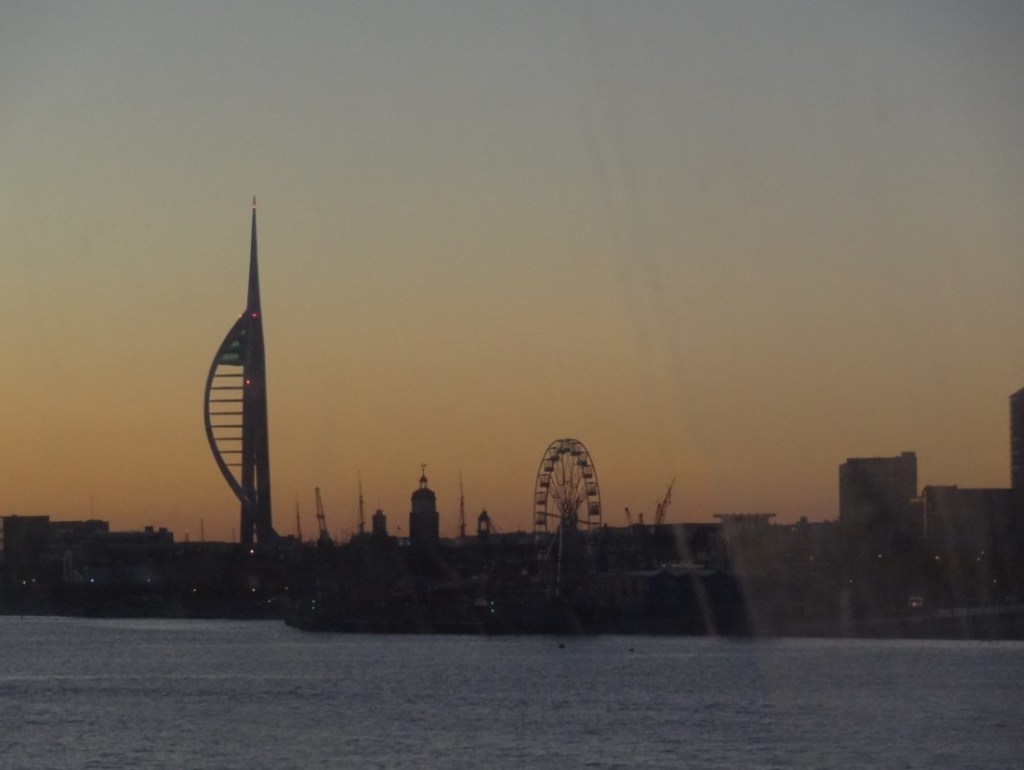 A sunset over a body of water with a city in the background

Description automatically generated